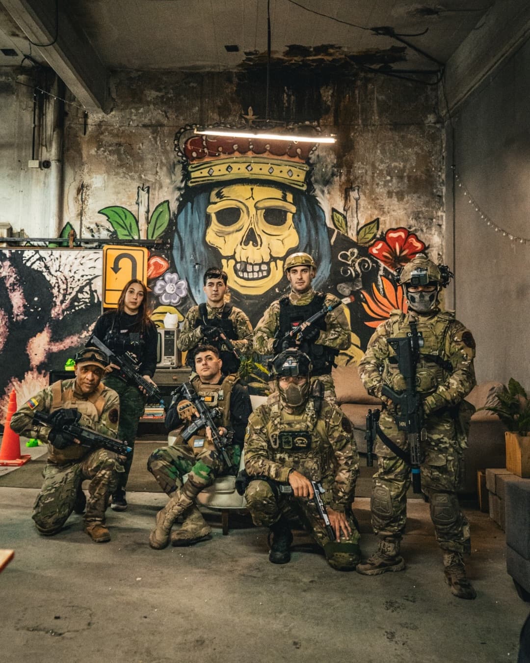 Grupo de jugadores equipados posando frente al mural de la calavera con corona dentro del complejo.